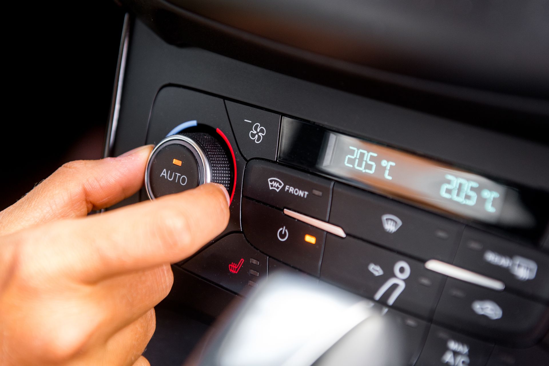 Une main règle le bouton de climatisation d’une voiture, dont l’affichage numérique indique 20,5 °C.