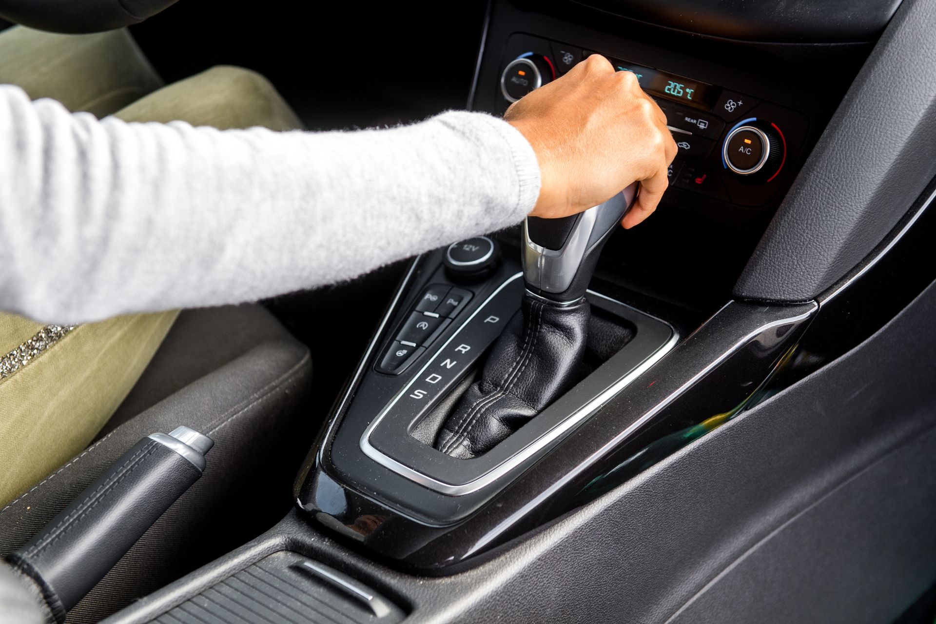 Main en train de passer les vitesses sur le levier automatique d’une voiture, dans la console centrale.