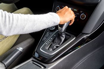 Main en train de passer les vitesses sur le levier automatique d’une voiture, dans la console centrale.