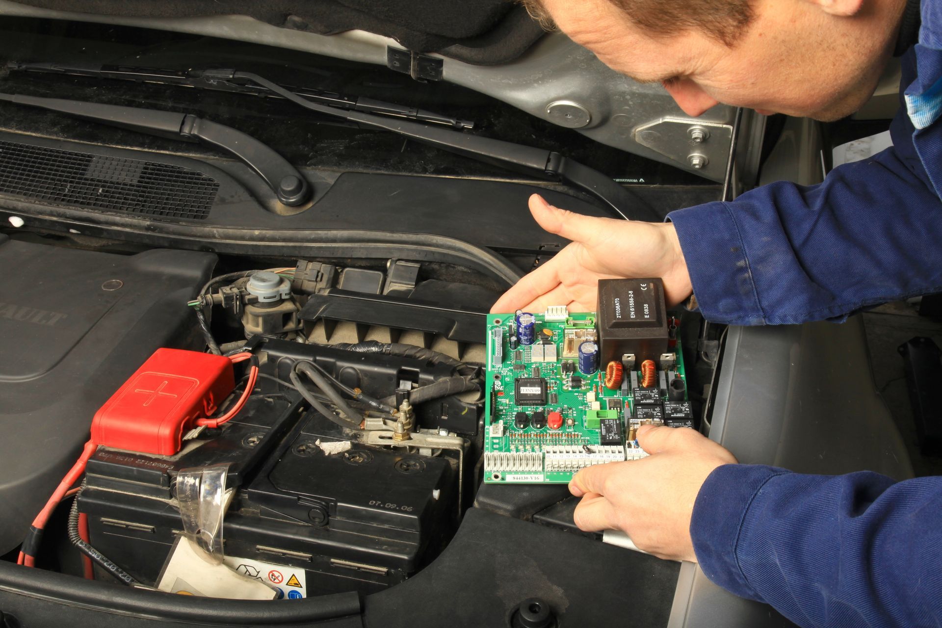Un mécanicien inspecte la batterie et les composants électroniques d’une voiture, avec un circuit imprimé sous le capot.