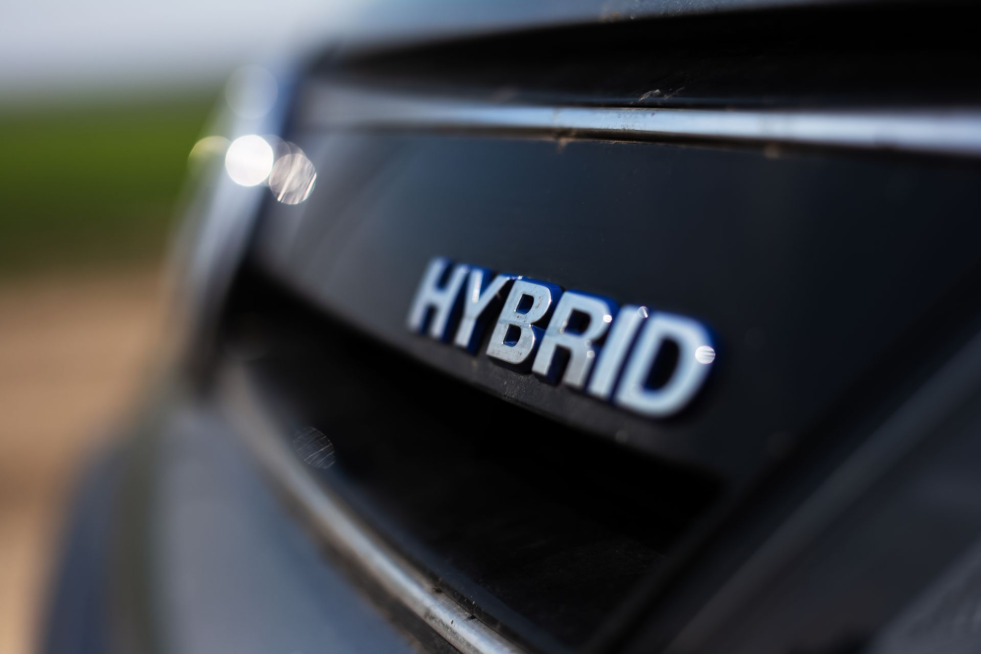 Gros plan sur l’inscription HYBRID du hayon d’une voiture, sur une surface noire.