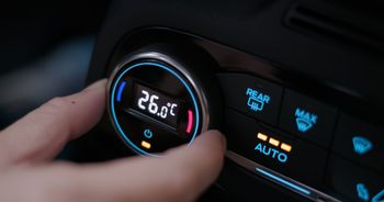 Une main règle le bouton de climatisation d’une voiture, avec un affichage de température rétroéclairé en bleu et des boutons de climatisation.