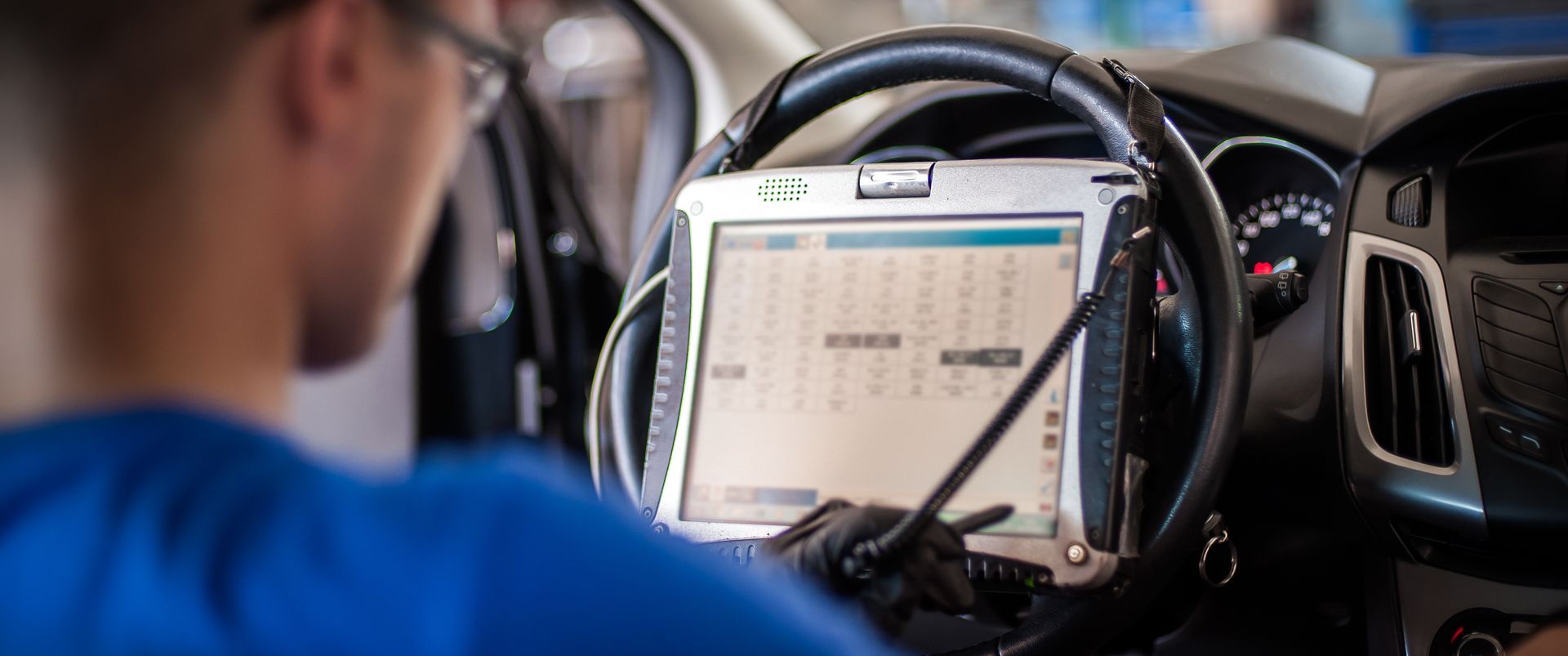 Personne en chemise bleue utilisant un ordinateur portable avec un volant monté à l’intérieur d’un véhicule.