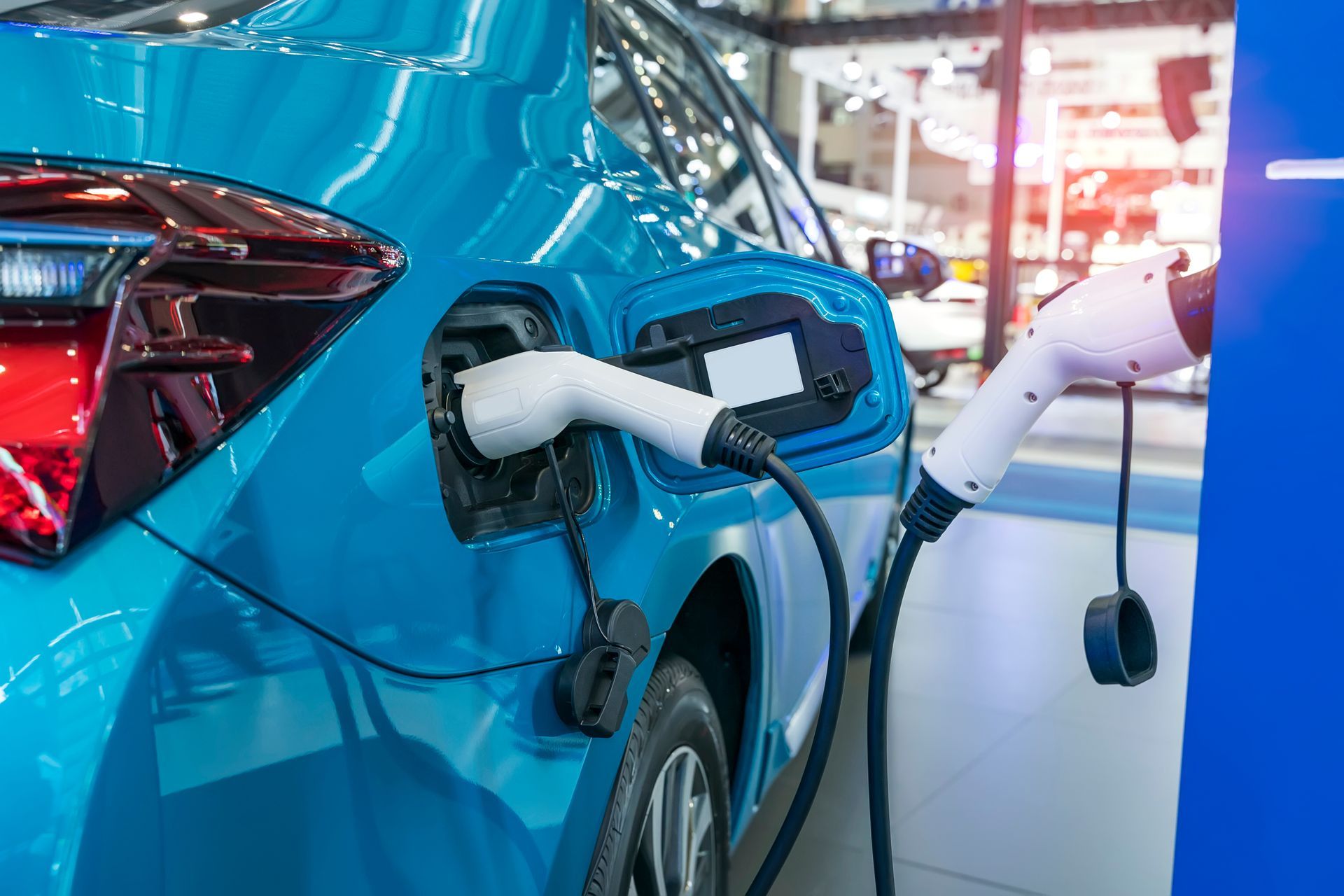 Voiture électrique bleue en cours de recharge avec une prise blanche sur une borne, gros plan sur l’arrière du véhicule.