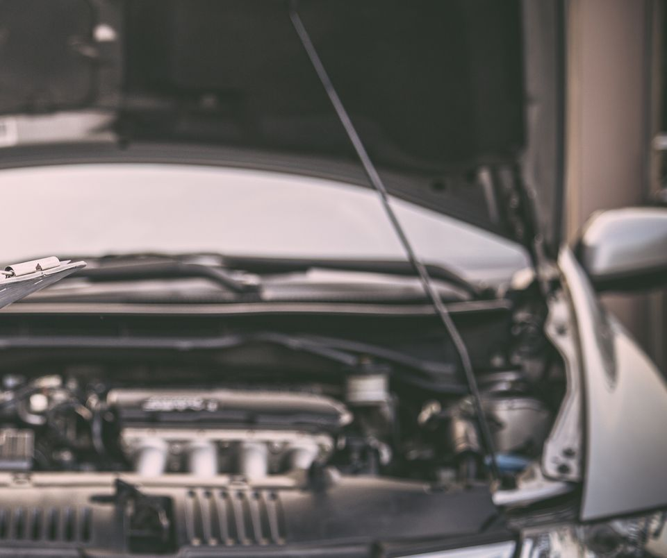 Capot de voiture ouvert, laissant apparaître le compartiment moteur dans un garage.