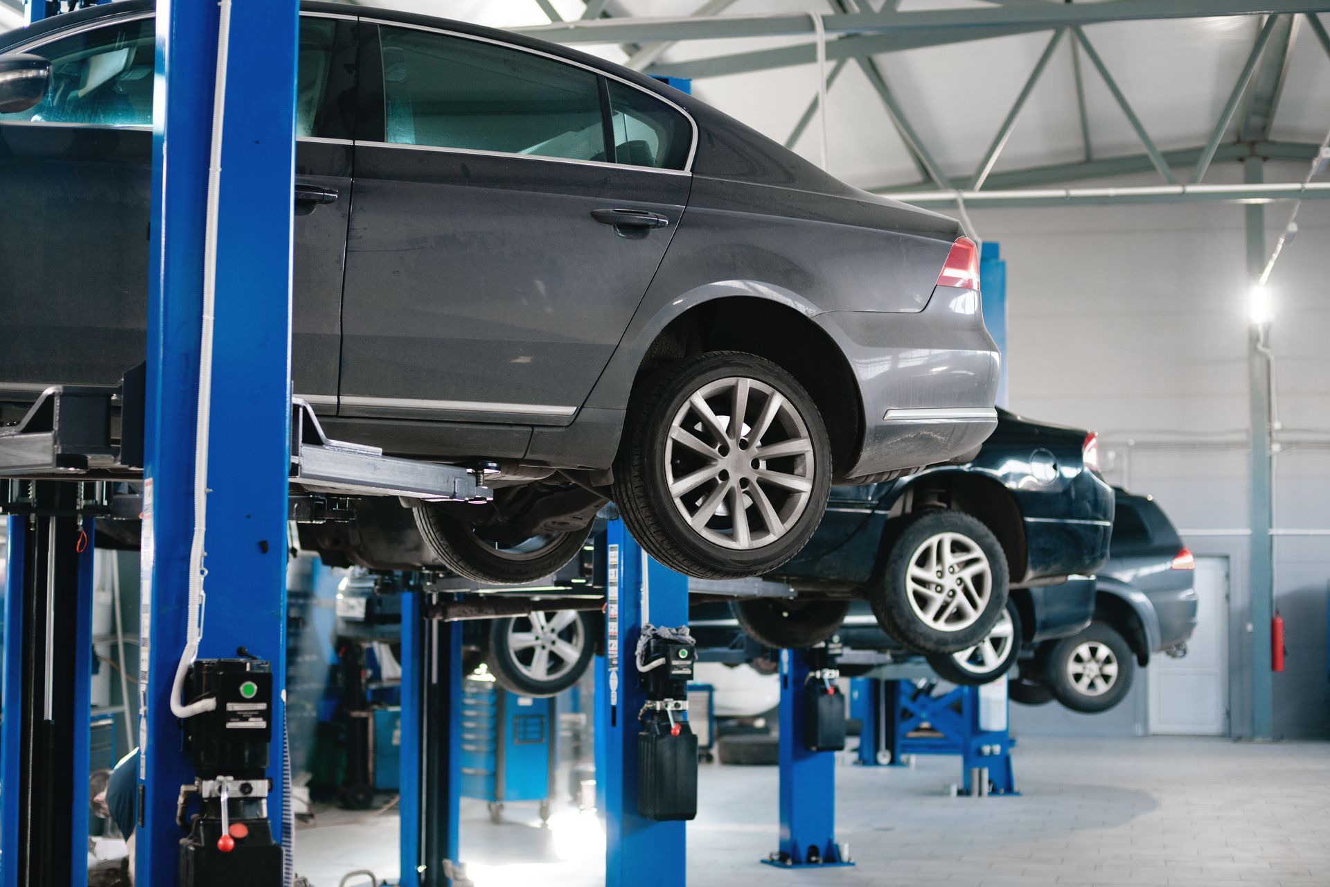 Voitures soulevées par des ponts élévateurs bleus dans un garage de réparation automobile.