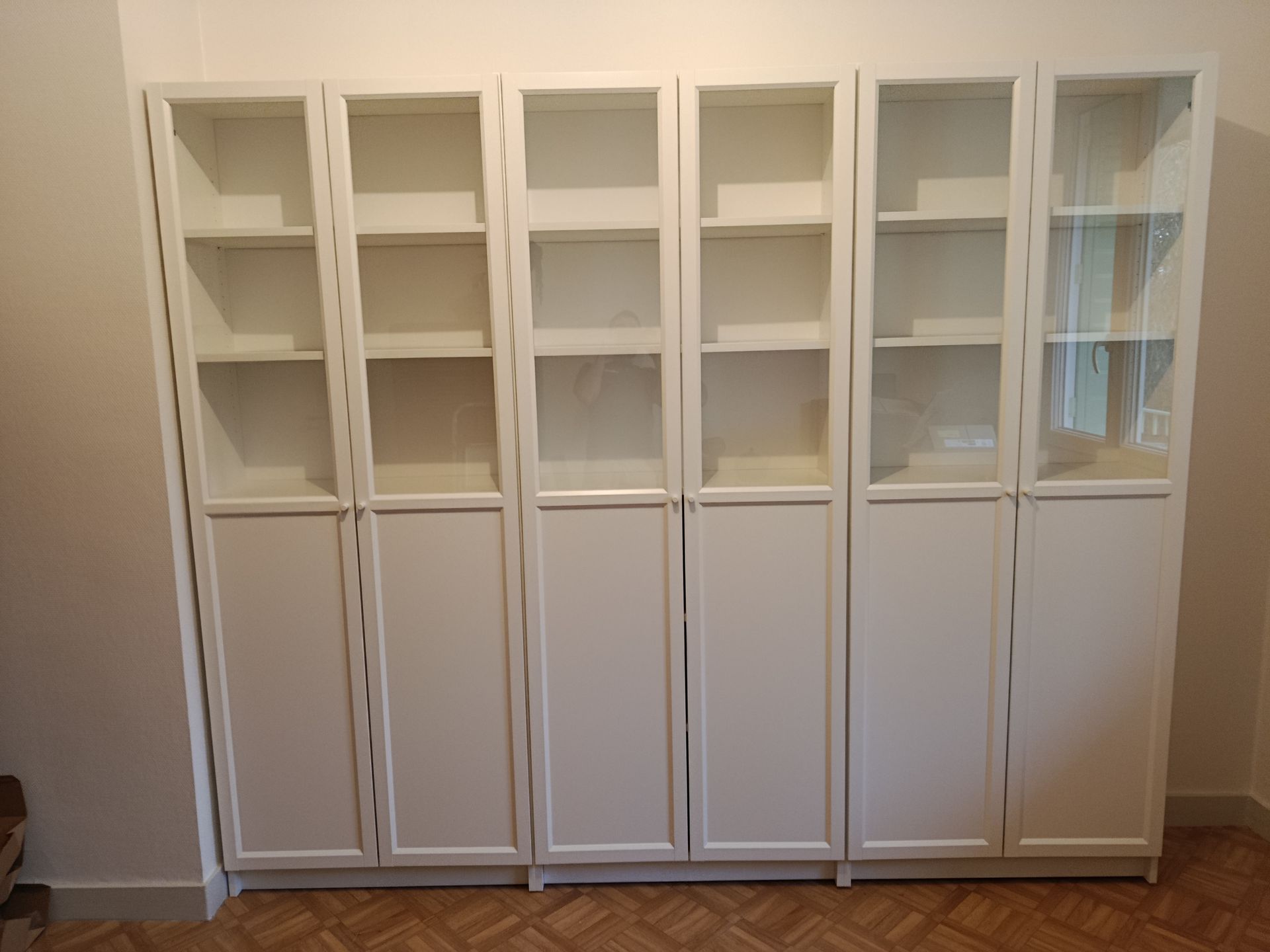 Une bibliothèque blanche allant du sol au plafond, avec des portes supérieures vitrées et des placards inférieurs pleins, adossée à un mur.