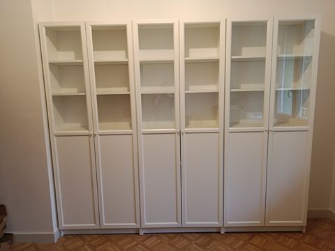 Une bibliothèque blanche allant du sol au plafond, avec des portes supérieures vitrées et des placards inférieurs pleins, adossée à un mur.