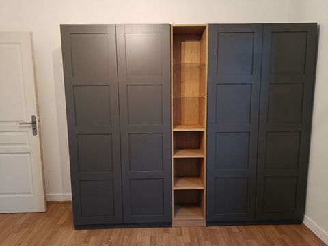 Une grande armoire à quatre portes gris foncé avec une colonne centrale d'étagères ouvertes en bois clair, posée sur un sol en bois.