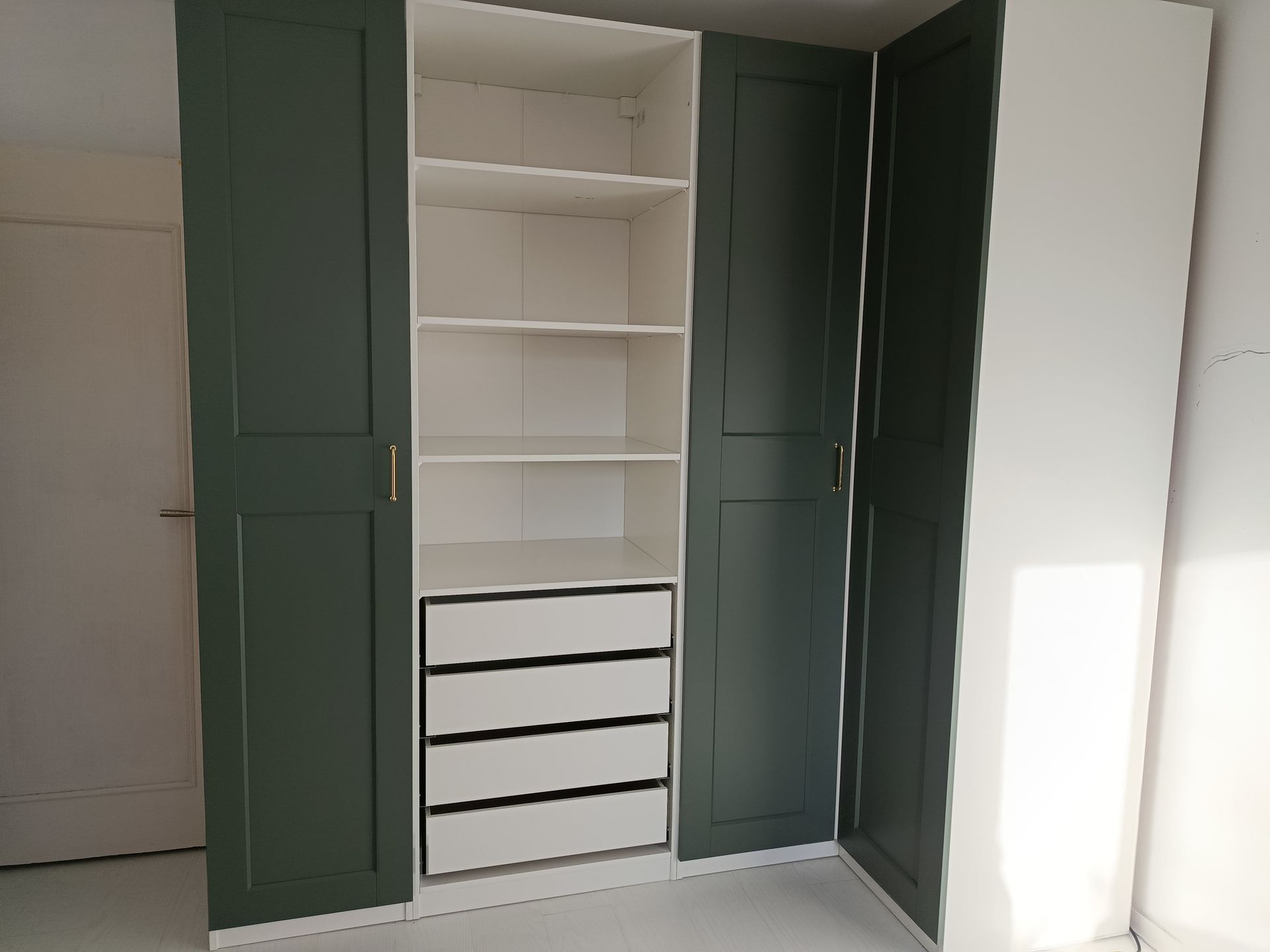 Une armoire modulaire avec des portes vert sombre encadrant une colonne centrale d'étagères ouvertes blanches et quatre tiroirs blancs.