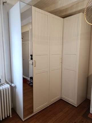 Une armoire d'angle blanche avec portes à panneaux et panneau latéral entièrement recouvert de miroir, dans une pièce avec parquet.