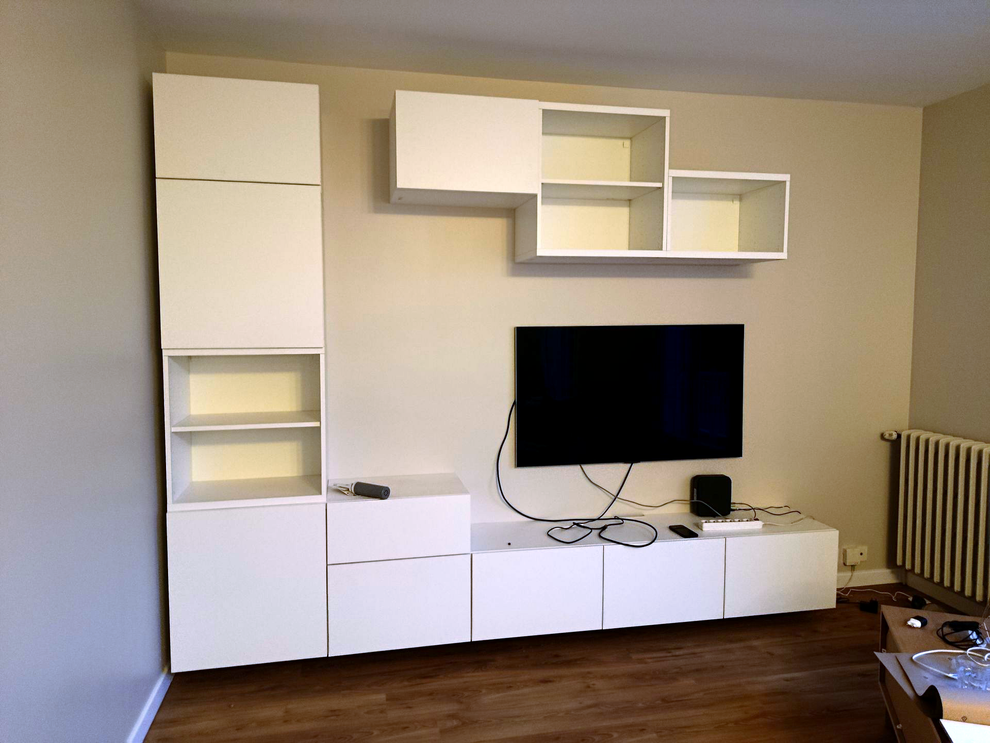 Meuble de rangement mural blanc moderne et étagères avec télévision à écran plat sur un mur beige dans une pièce avec parquet.