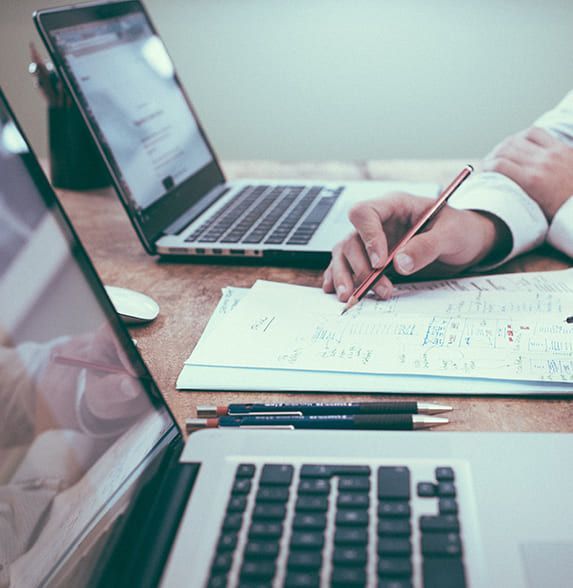 Employé à son bureau qui consulte des documents avec en face un ordinateur portable ouvert
