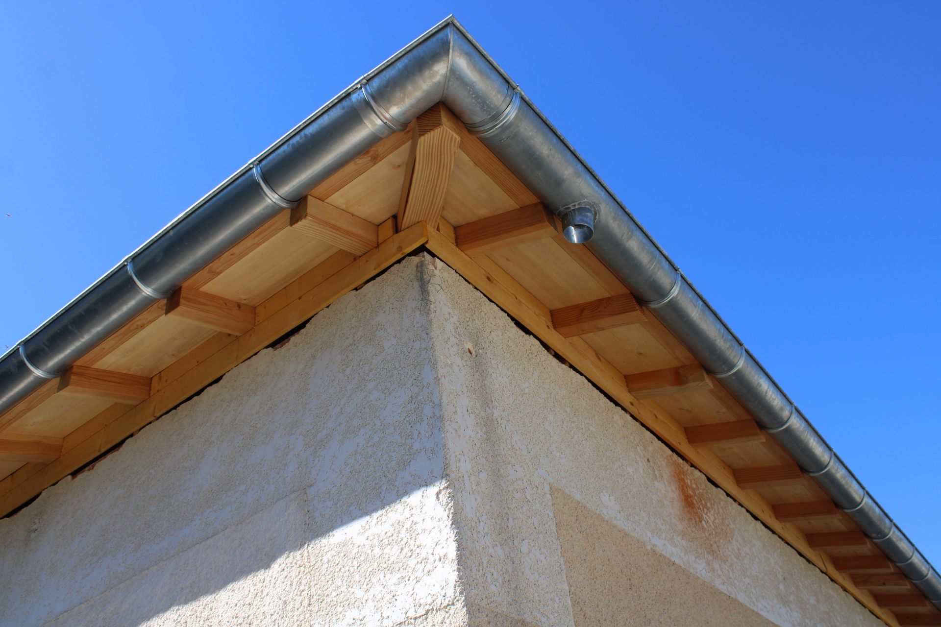 Coin de toit de maison avec gouttière grise sur fond de ciel bleu éclatant