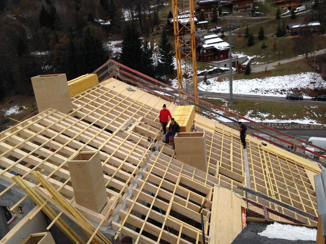 Des ouvriers charpentent le toit en pente d'une maison en construction, avec la neige en arrière-plan.