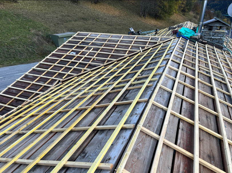 Toiture en construction avec chevrons en bois et liteaux jaunes sur une charpente à forte pente