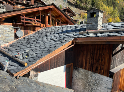 Chalets en bois au toit de pierre, à flanc de montagne, avec cheminée et tuiles saupoudrées de neige
