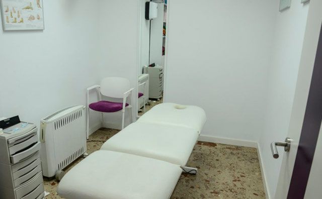 Una mesa de masajes blanca se encuentra en una pequeña habitación al lado de una silla.