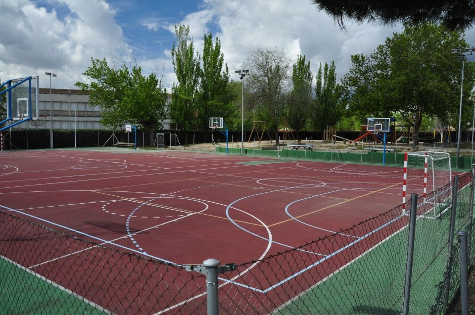 Pista deportiva al aire libre con canastas de baloncesto y porterías de fútbol, ​​cercada, bajo un cielo nublado.