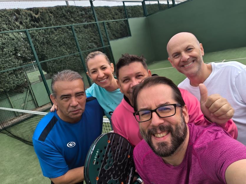 Grupo de cinco personas sonriendo en una pista de pádel; dos de ellas sostienen una raqueta.