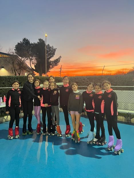 Un grupo de patinadores, con trajes iguales, posa para una foto al anochecer en una pista azul.