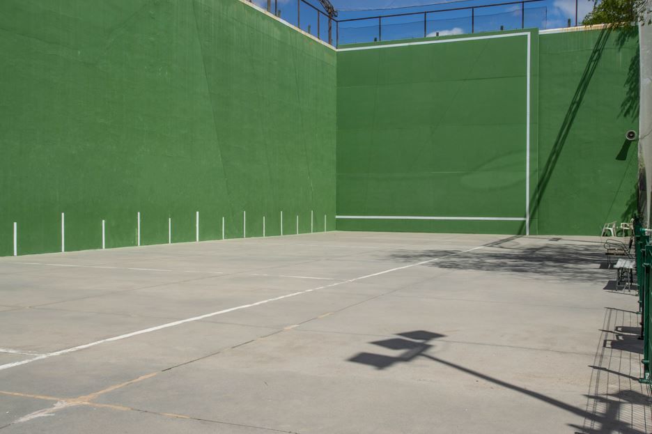 Una cancha de balonmano verde con líneas blancas y un muro alto, iluminada por la luz del sol.