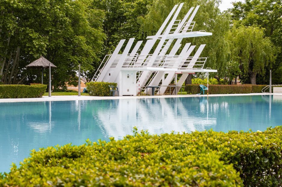 Piscina con trampolín blanco. Rodeada de exuberante vegetación.