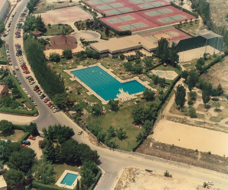 Vista aérea de un complejo deportivo con pistas de tenis, piscinas y un edificio en un día soleado.
