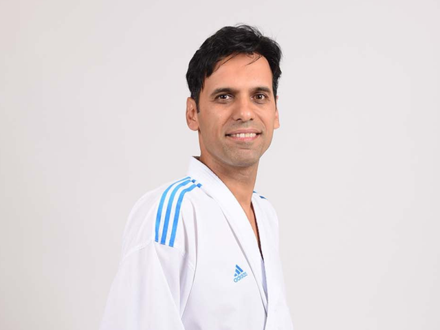 Mann in weißer Adidas-Uniform mit blauen Streifen lächelt in einem Studio.