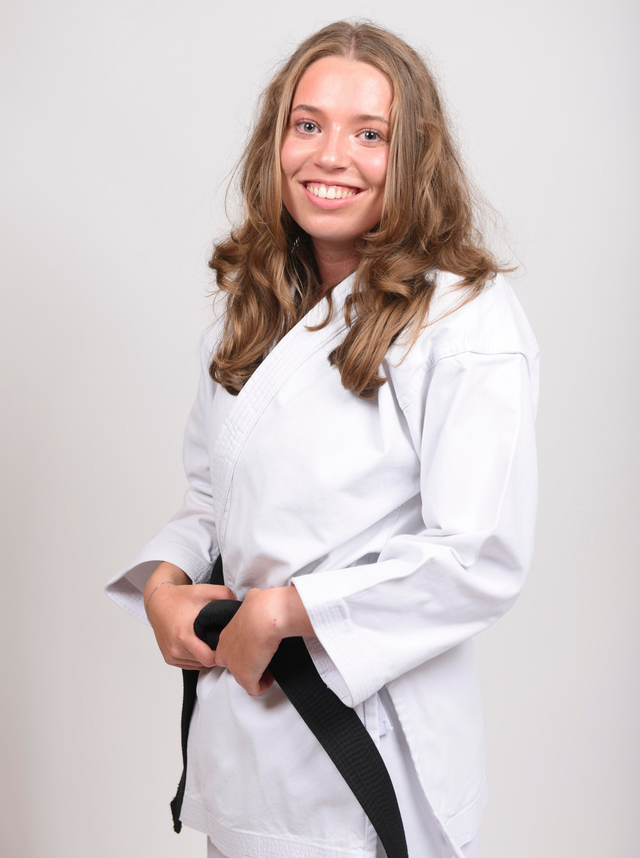 Frau in weißer Karateuniform und schwarzem Gürtel, lächelnd.