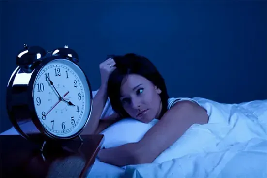 Una mujer está acostada en la cama mirando un despertador.