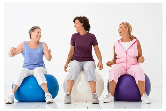 Tres mujeres están sentadas sobre pelotas de ejercicio y ríen.