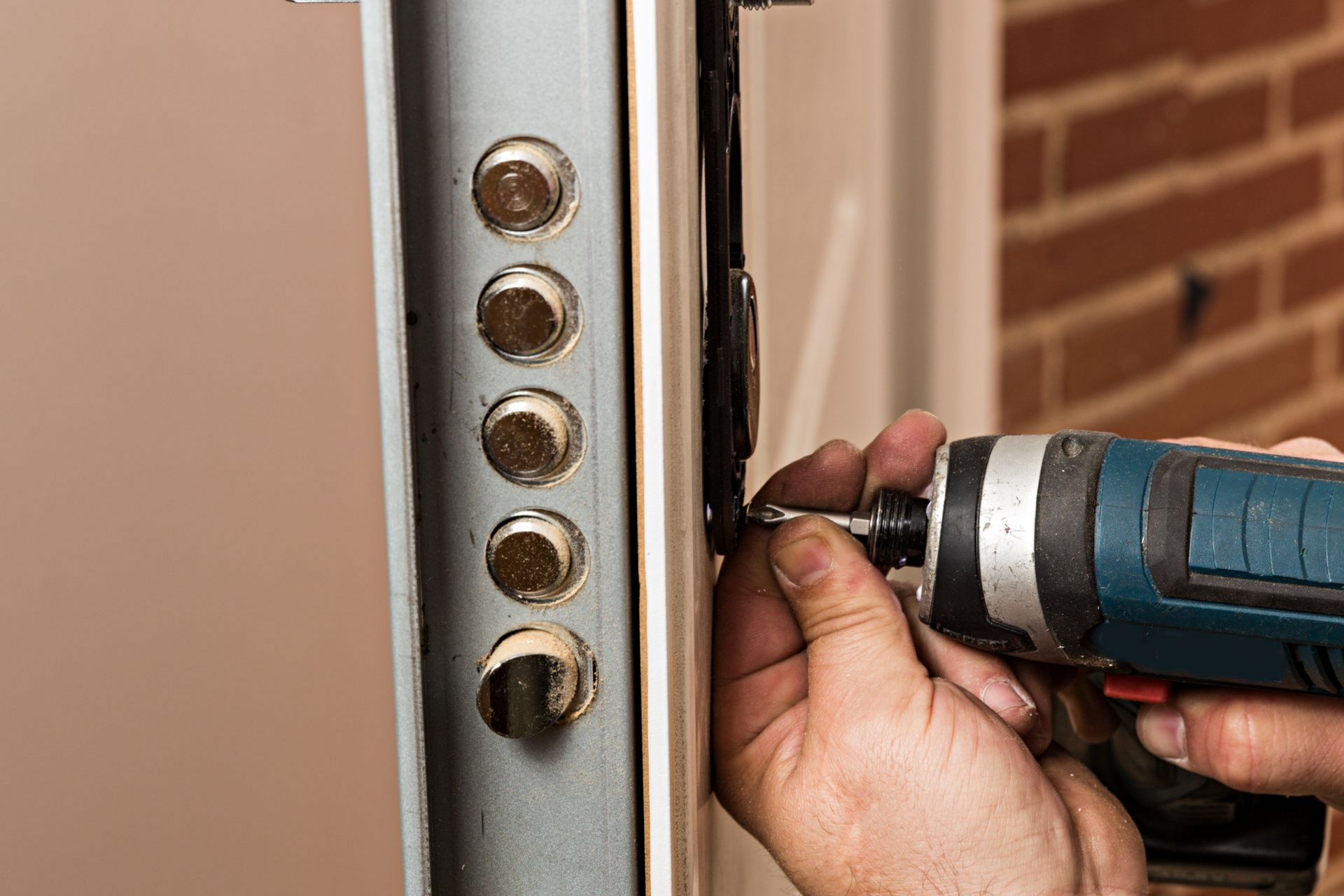 Une personne utilisant une visseuse électrique pour installer ou réparer une serrure sur une porte beige.