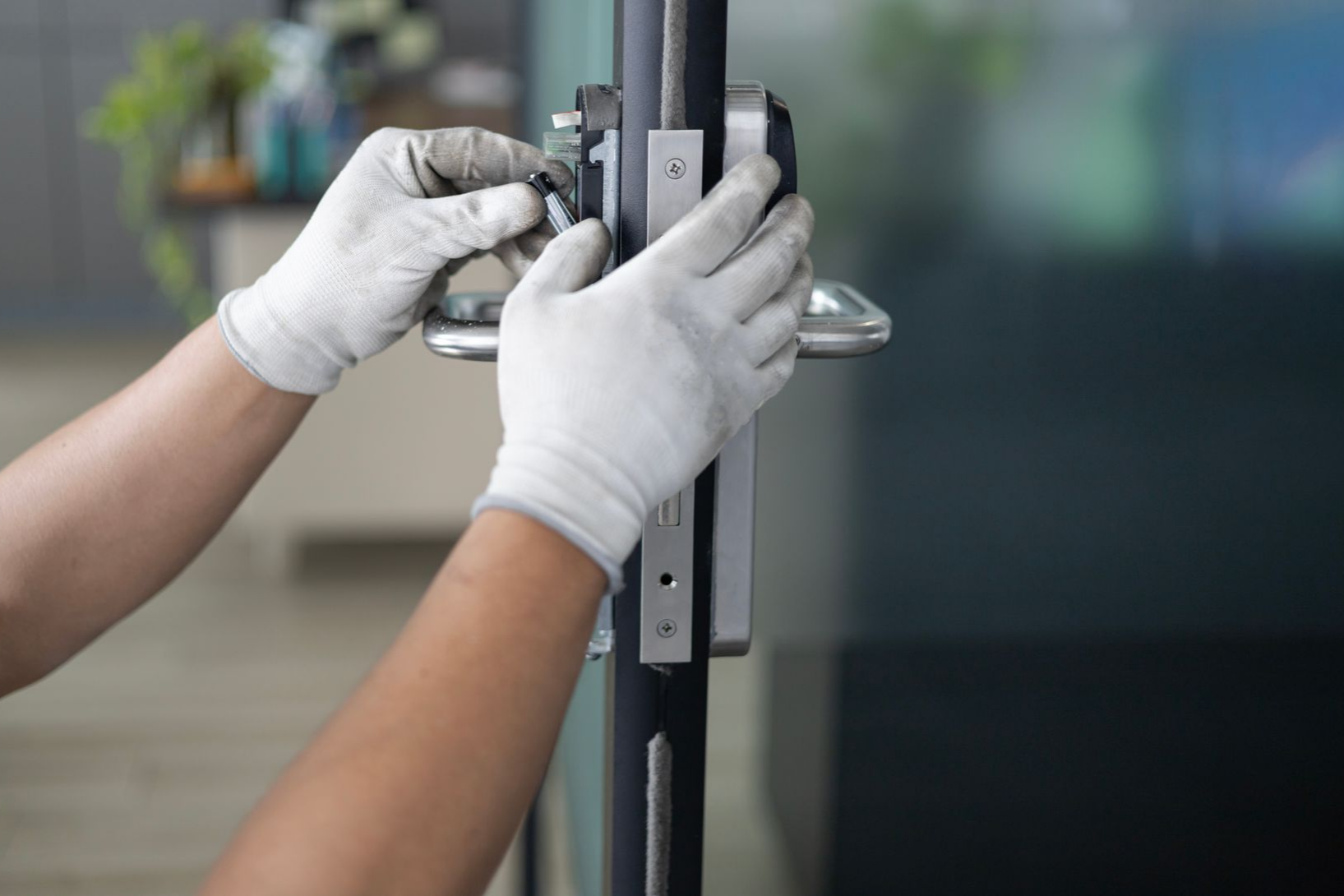 Une personne portant des gants installe des ferrures sur une porte vitrée.