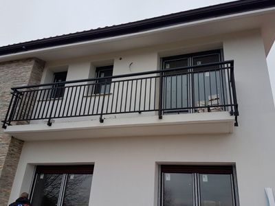 Un balcón en el costado de una casa blanca con una barandilla negra.