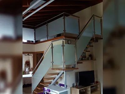 Una sala de estar con escalera y barandilla de cristal.