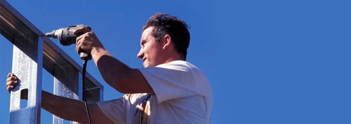 Un hombre está trabajando en una valla con un taladro.