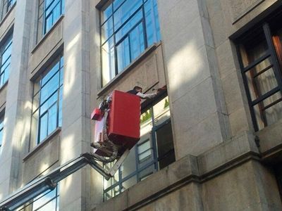 Un hombre está en un cubo rojo al costado de un edificio.