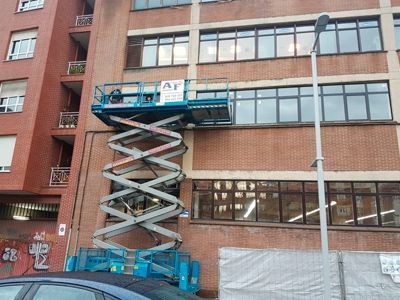 Un elevador de tijera azul está estacionado frente a un edificio de ladrillos.