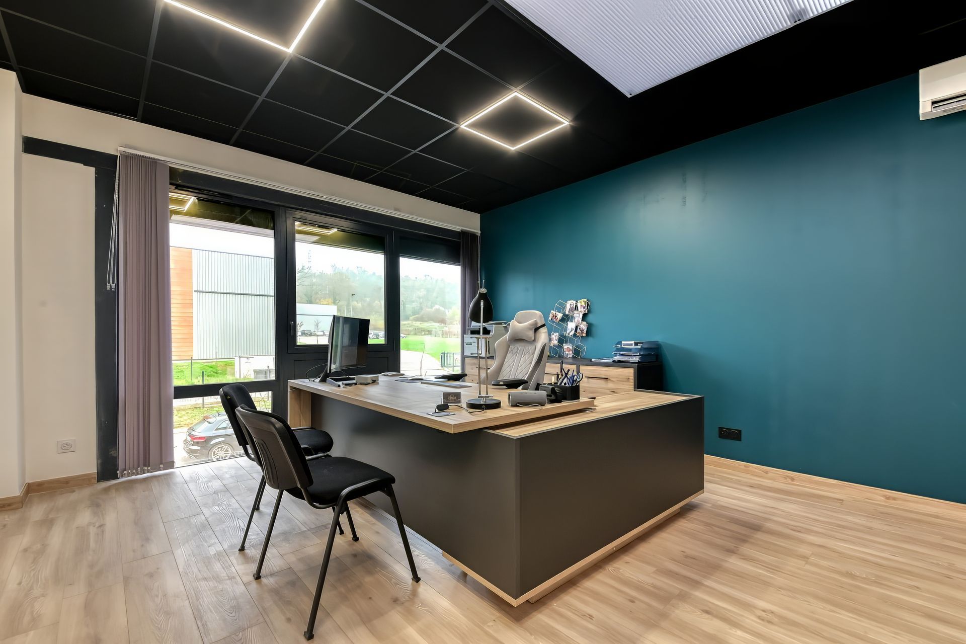 Bureau moderne avec un mur d'accent turquoise, un bureau, des chaises noires et des luminaires carrés au plafond.