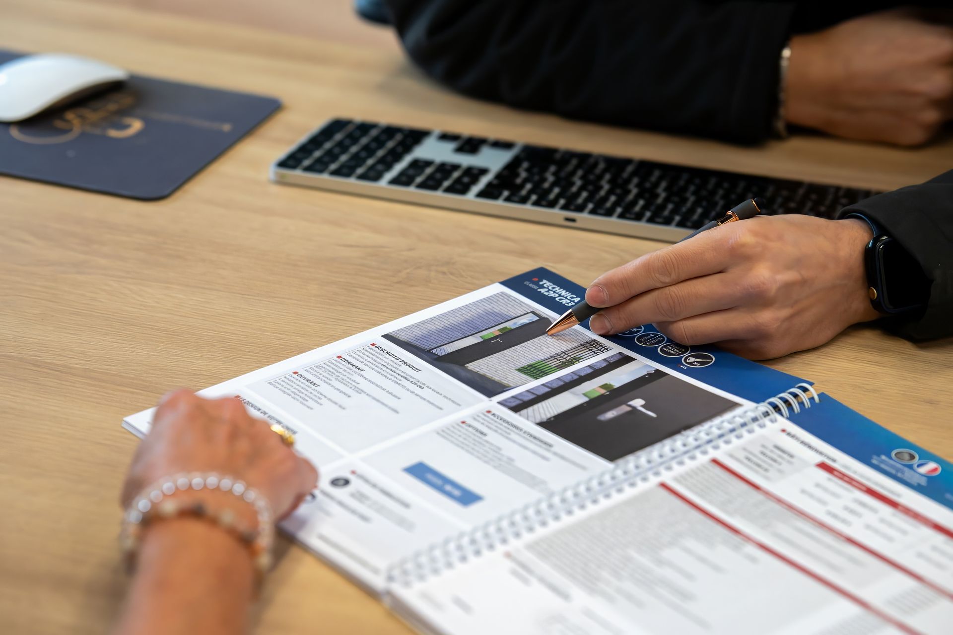 Deux personnes examinent un document à un bureau, avec un clavier et une souris à proximité.