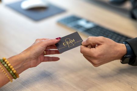 Des mains échangent une carte de visite noire à lettres dorées à un bureau