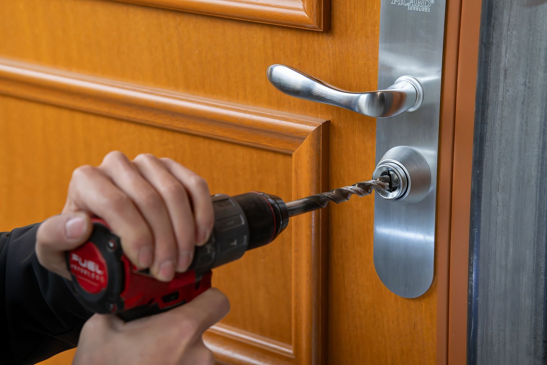 Une personne utilise une perceuse pour endommager la serrure d'une porte en bois.