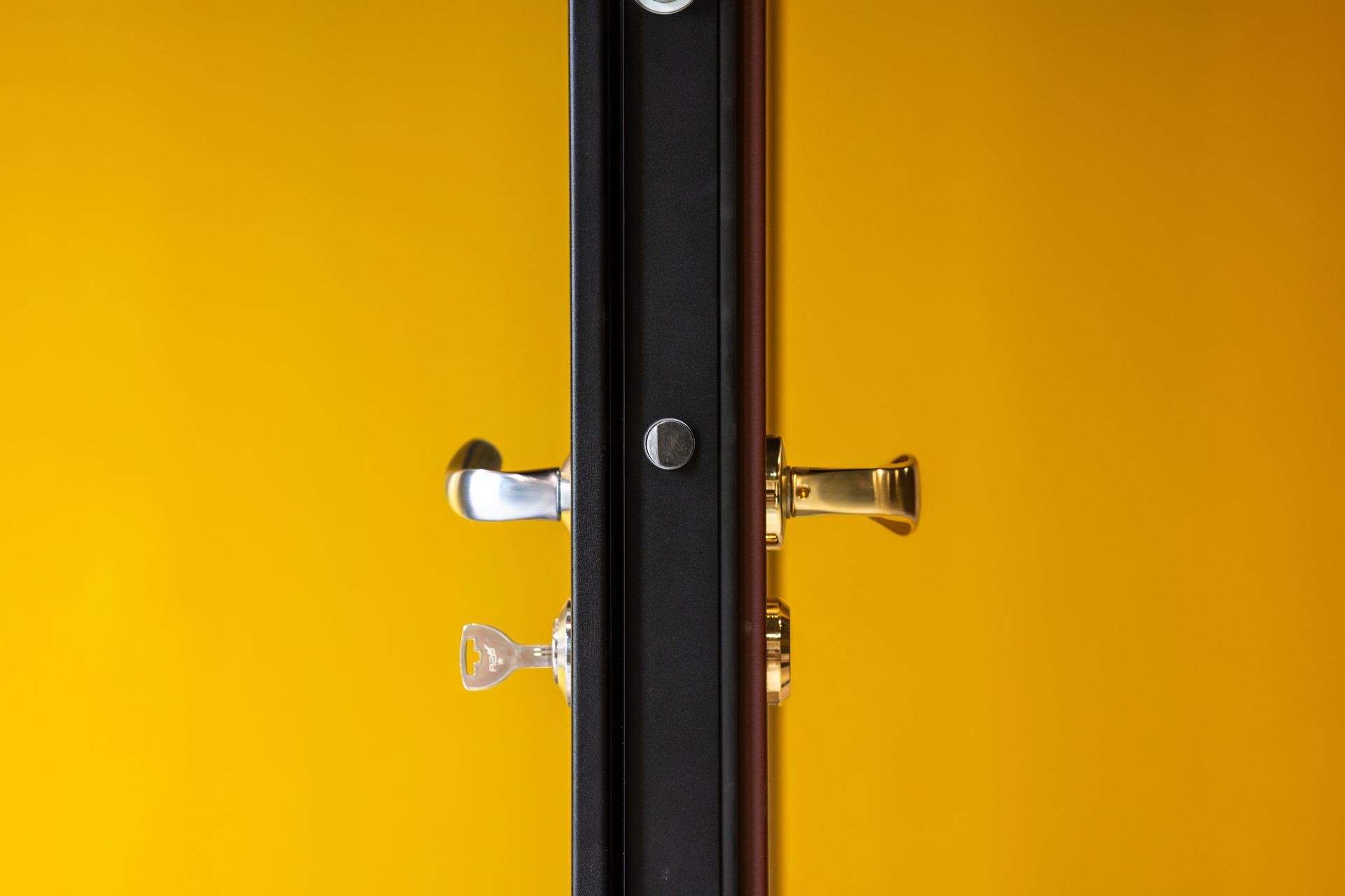 Cadre de porte noir avec poignées de porte argentées et dorées sur fond jaune.