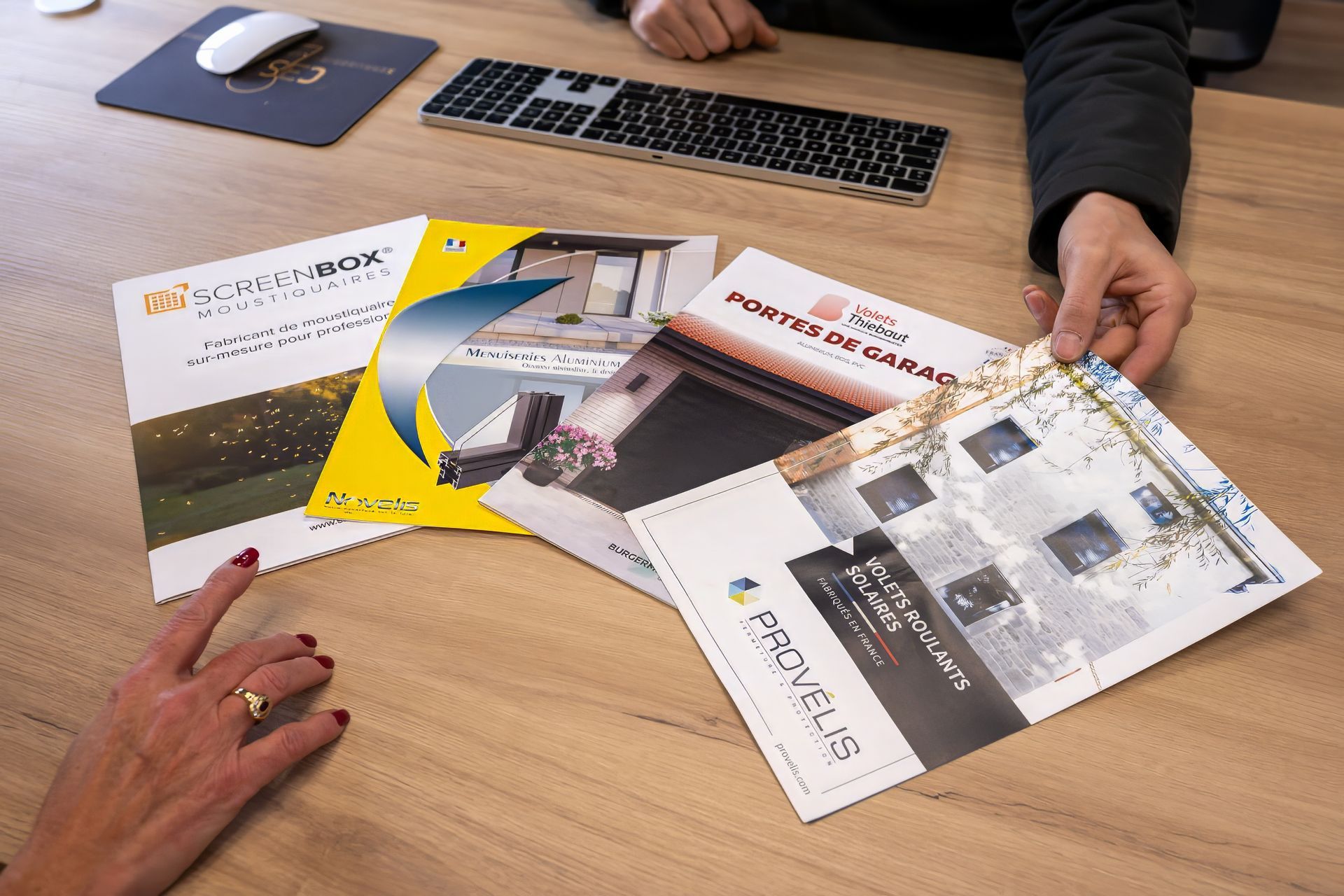 Des mains tiennent et désignent plusieurs brochures posées sur une table en bois