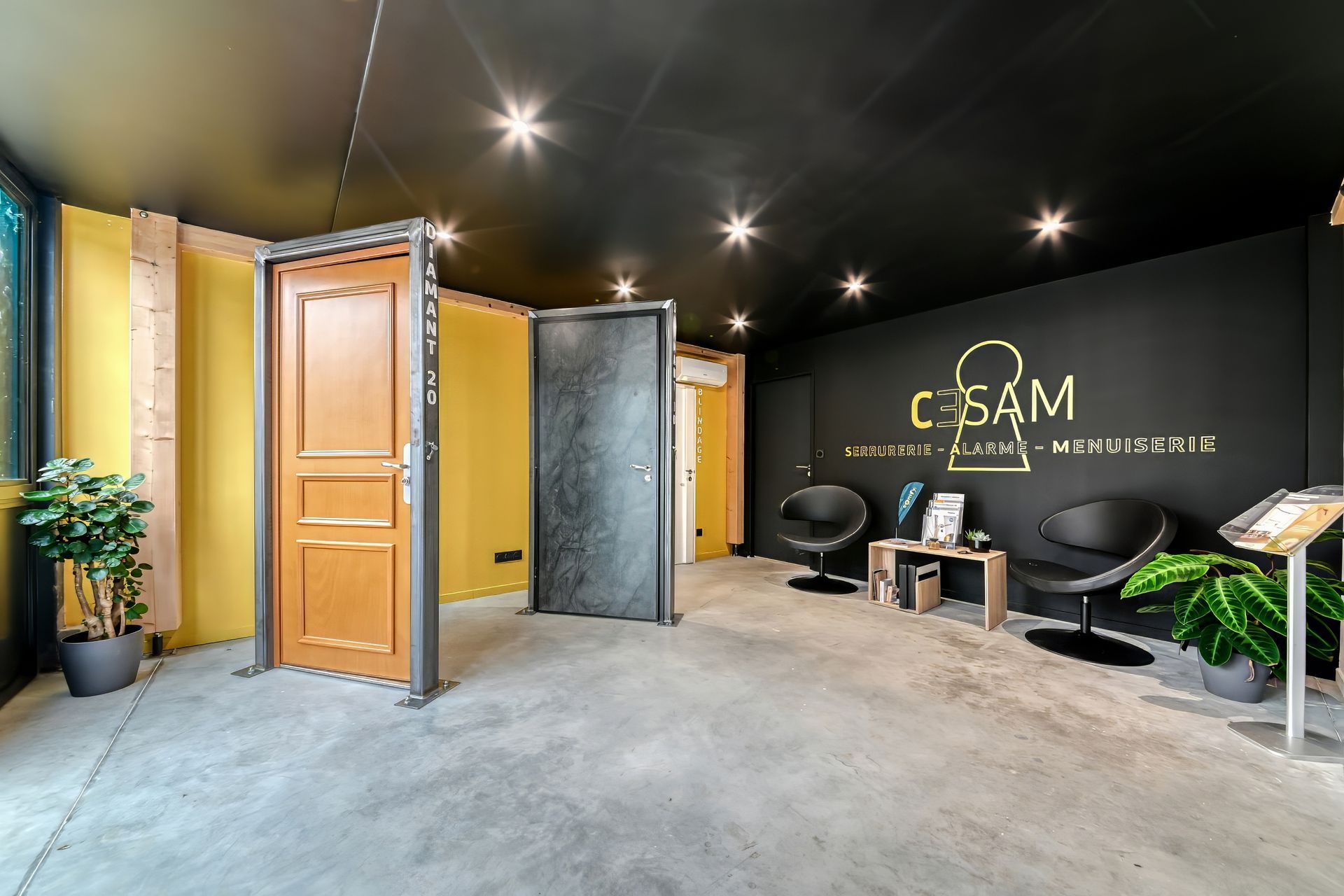 Salle d'exposition intérieure avec portes exposées, plafond noir, murs jaunes et noirs, coin salon et plantes.