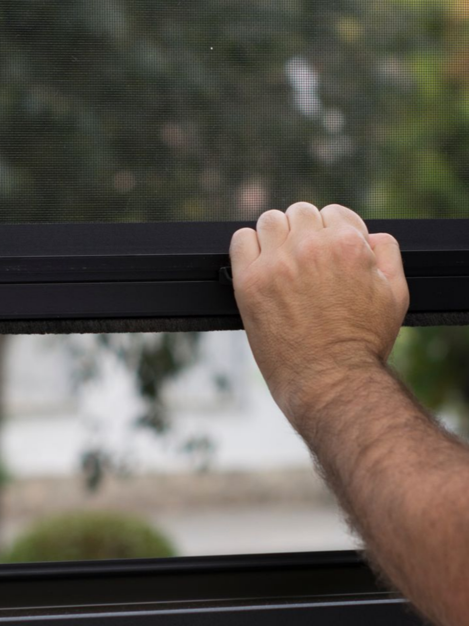 Une main agrippe un cadre de fenêtre noir pour l'ouvrir, avec un écran en arrière-plan.