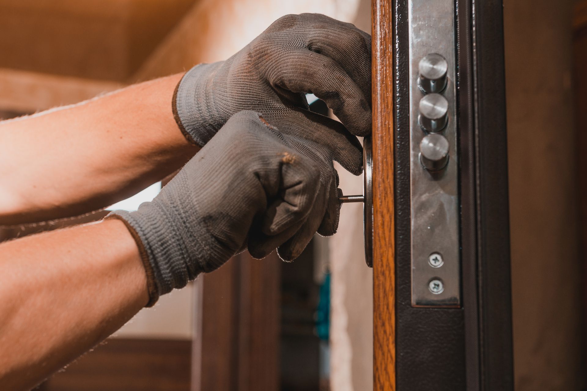 Des mains gantées installent une serrure sur un cadre de porte en bois