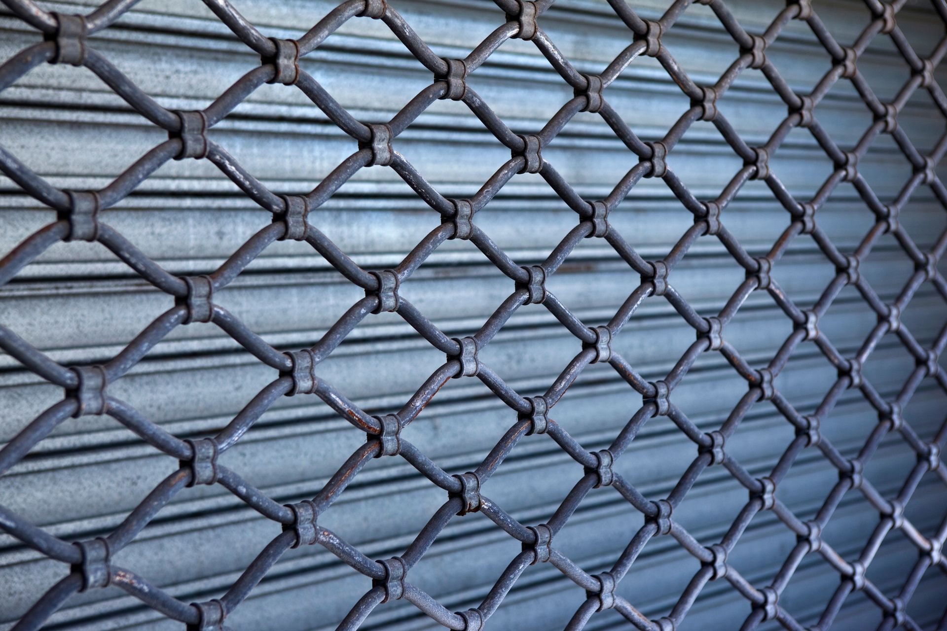 Grille de sécurité métallique à motif losange sur une surface métallique ondulée.