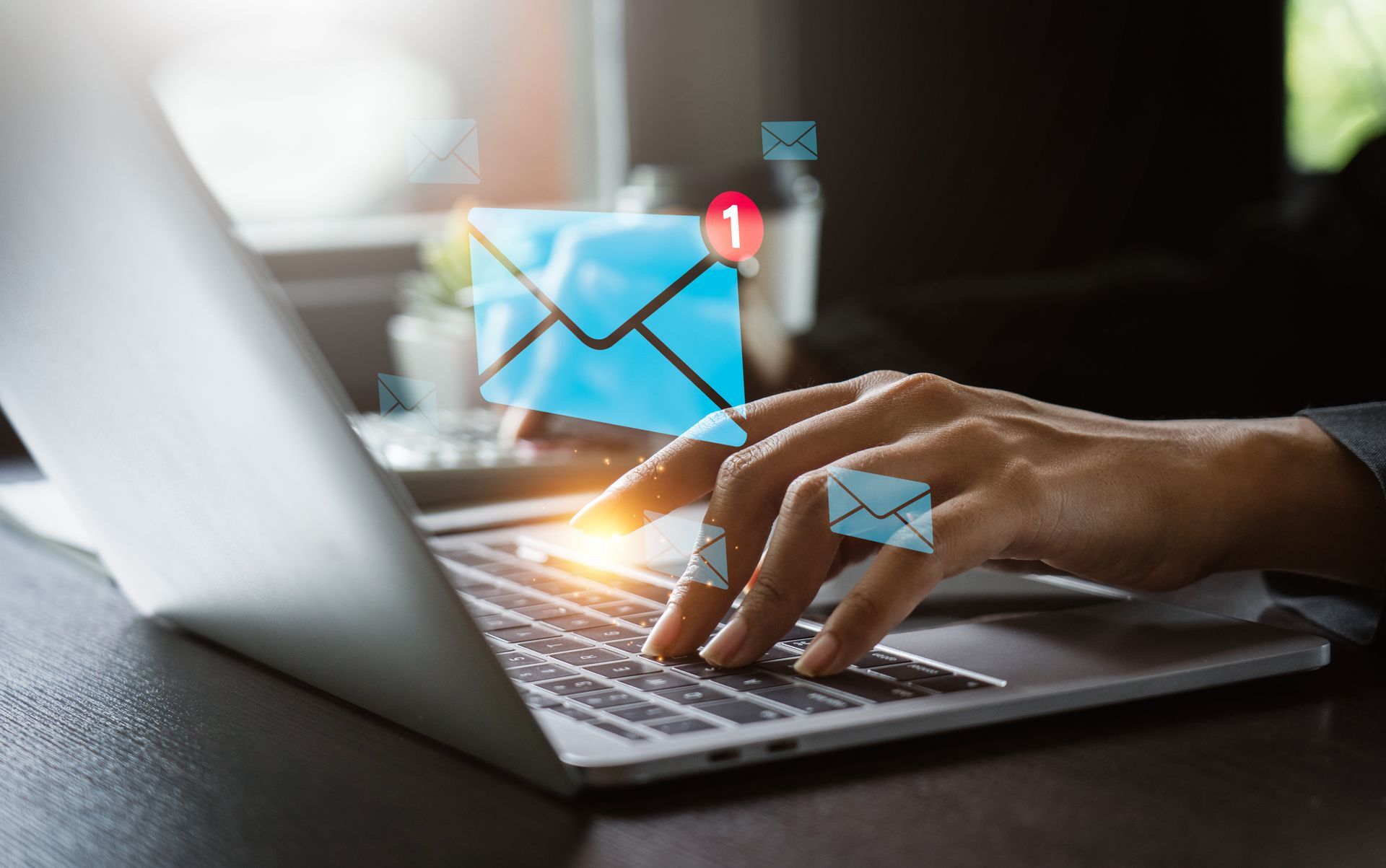 Persona escribiendo en un portátil con iconos de correo flotantes, lo que sugiere comunicación por email e interacción digital.